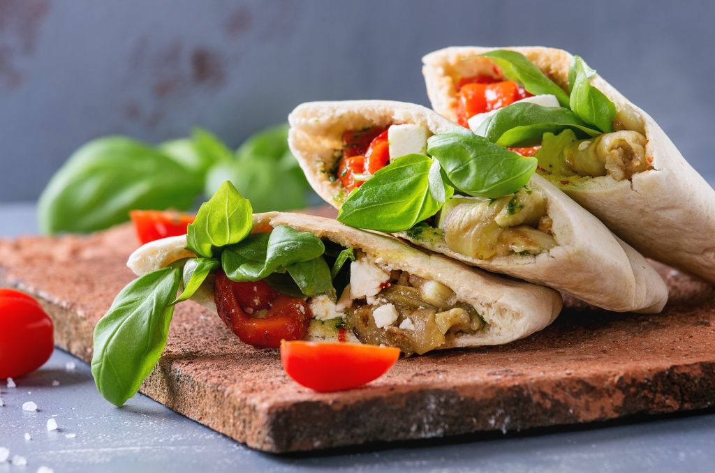 bigstock–181614709(1) Pita bread sandwiches with grilled vegetables paprika, eggplant, tomato, basil and feta cheese served on terracotta board over gray stone background. Close up. Healthy fast food concept.