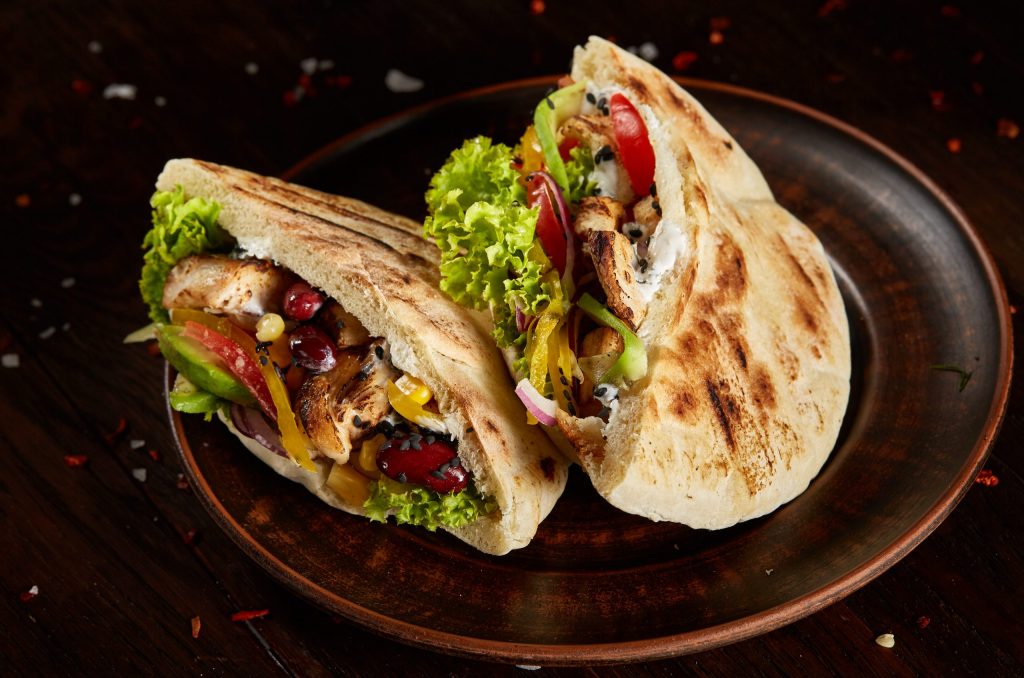 Tasty Jewish Pita Stuffed With Grilled Chicken, Vegetables, Bean Tasty Jewish pita stuffed with grilled chicken, vegetables, beans, letucce on old-fashioned plate over vintage wooden background, side view, close-up, selective focus. Organic stuffed roll. Traditional Middle East cuisine. Fast food concept.