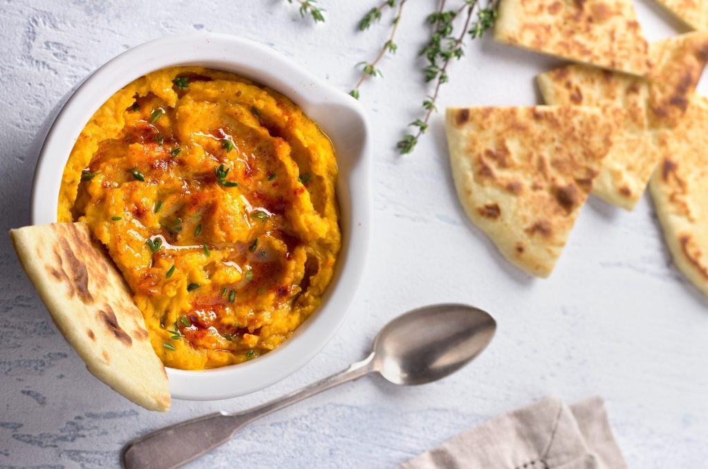 Delicious Healthy Homemade Bean Hummus With Baked Pumpkin, Tahin Delicious healthy homemade bean hummus with baked pumpkin, tahina and spices with flat bread on a light blue background, top view